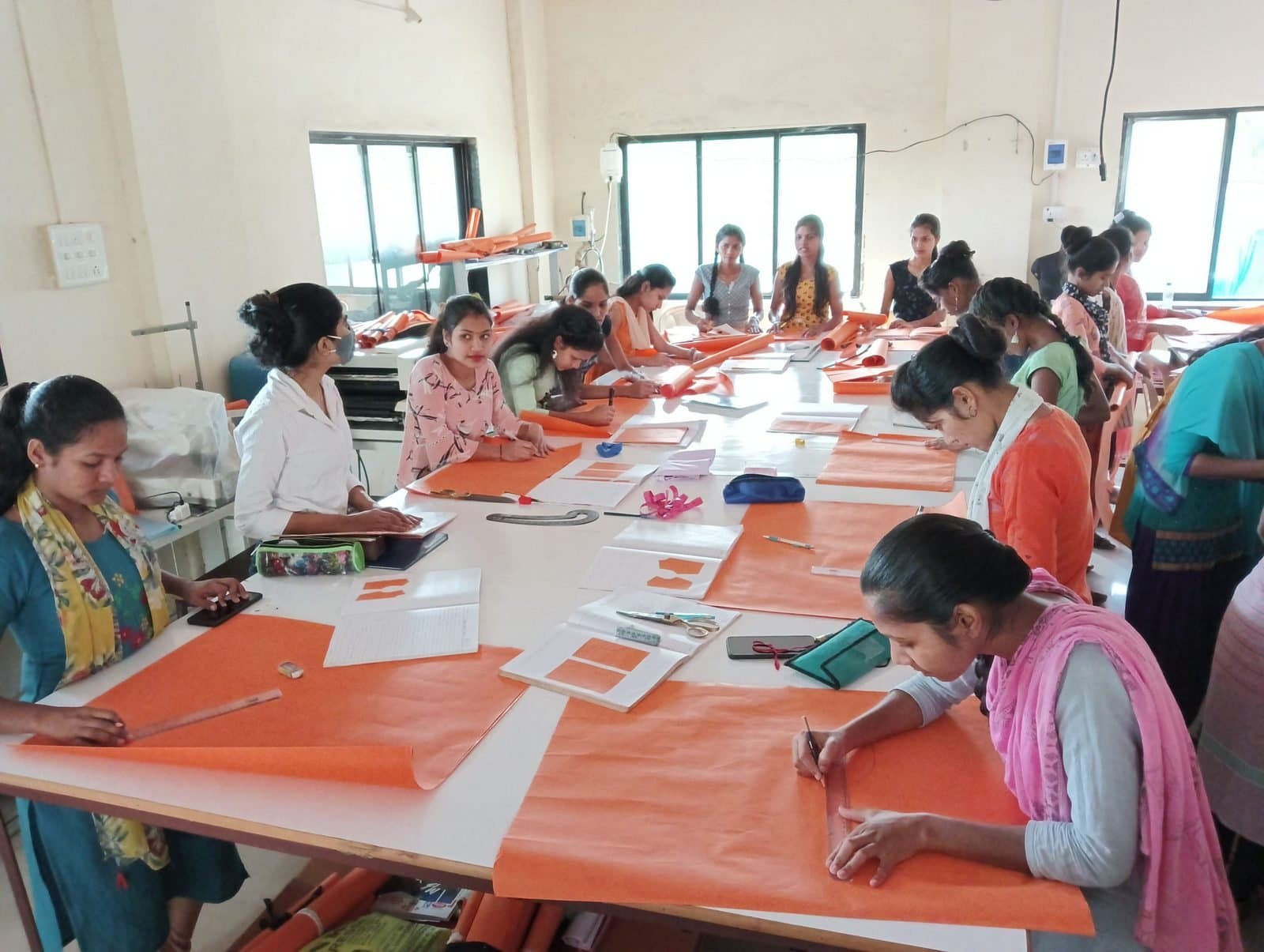 Design students drafting patterns on paper at long studio tables