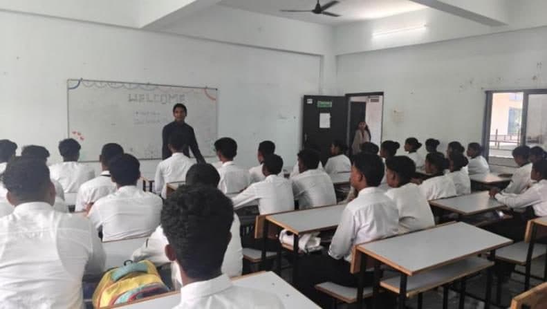 Students in uniform listening to a guest lecture in a classroom