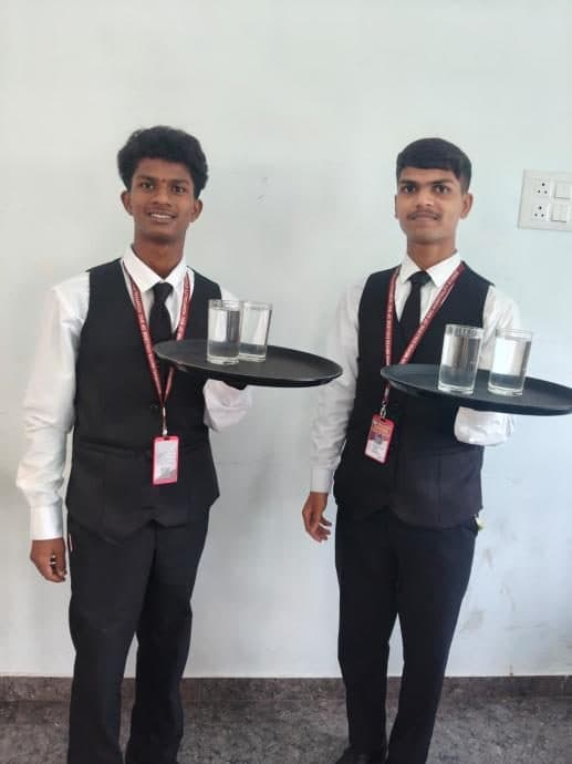 Two students carrying service trays with glasses