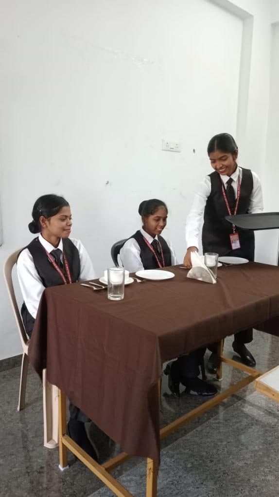 Students practising table service with seated guests
