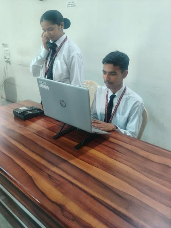 Students at a reception desk with a laptop and telephone during a front office practical