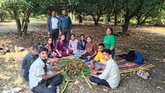 Students and staff sitting together under trees for ukadhandi and vanbhojan