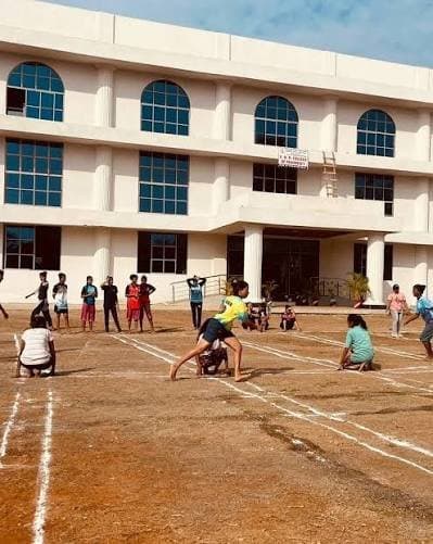 Students playing kho-kho on the ground in front of a college building